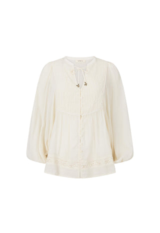 an-off-white-long-sleeve-blouse-with-a-tie-neck-detail-vertical-pleats-on-the-bodice-and-lace-trim-at-the-hem-shown-against-a-plain-white-background