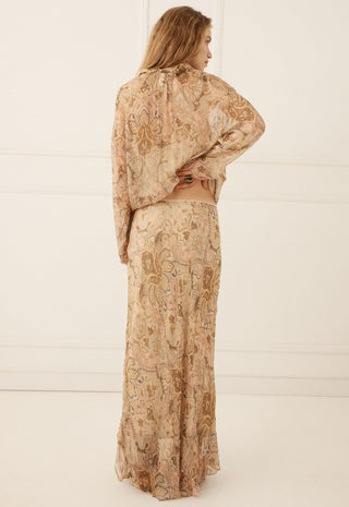 a-woman-stands-with-her-back-to-the-camera-wearing-a-matching-two-piece-set-consisting-of-a-long-sleeve-cropped-top-and-a-long-skirt-both-in-a-beige-and-brown-paisley-patterned-fabric