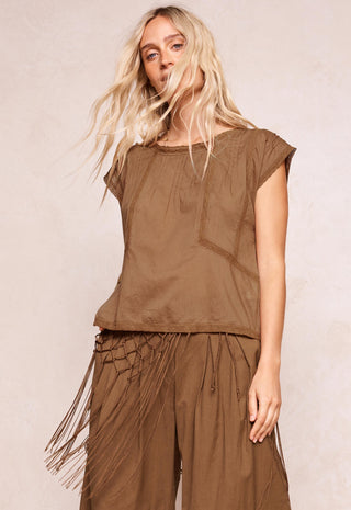 A woman modeling a brown short-sleeve top and matching wide-leg pants with fringe details, set against a neutral beige background.