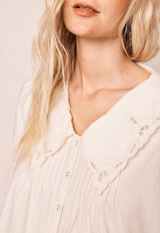 close-up-of-a-woman-wearing-a-cream-colored-blouse-with-a-large-scalloped-eyelet-collar-and-button-front