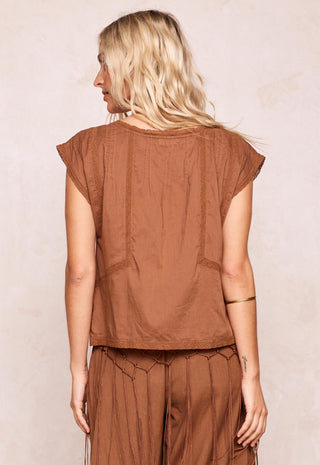 A woman shown from the back wearing a brown short-sleeve top and matching brown pants against a light beige textured wall.