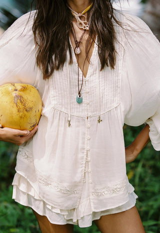 A woman wearing a loose white bohemian-style blouse with ruffled trim and front buttons, holding a yellow coconut outdoors.