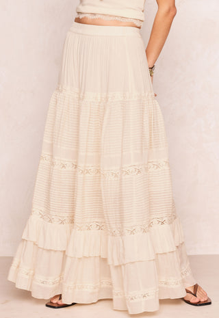a-long-cream-colored-tiered-maxi-skirt-with-delicate-lace-trim-and-ruffles-shown-on-a-model-from-the-waist-down-against-a-light-textured-wall