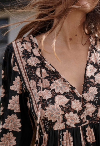 Close-up of a woman wearing a black V-neck dress with a beige and pink floral print, styled with a matching crossbody bag.