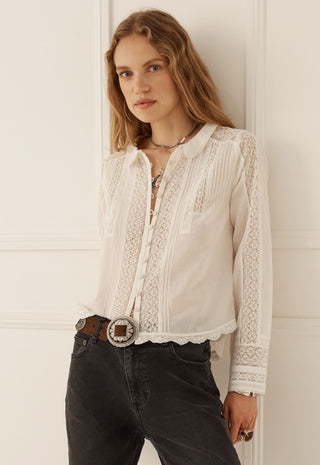 A woman wearing a white long-sleeve blouse with intricate lace and embroidered detailing